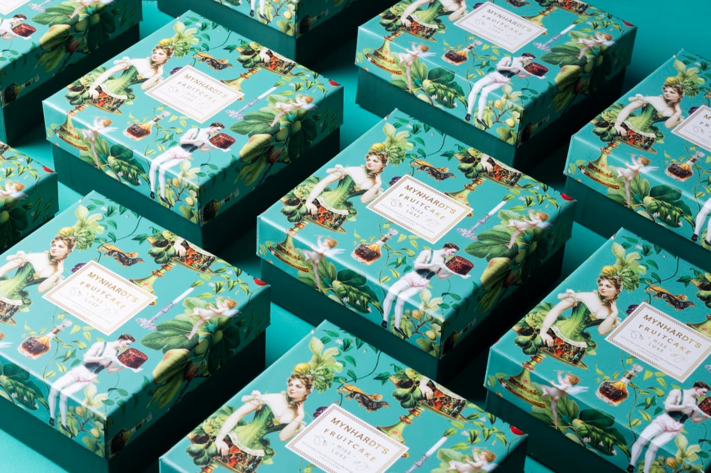 Rows of Miss Luxe fruitcake boxes in teal illustrated wrapping, photographed from above on a teal ground