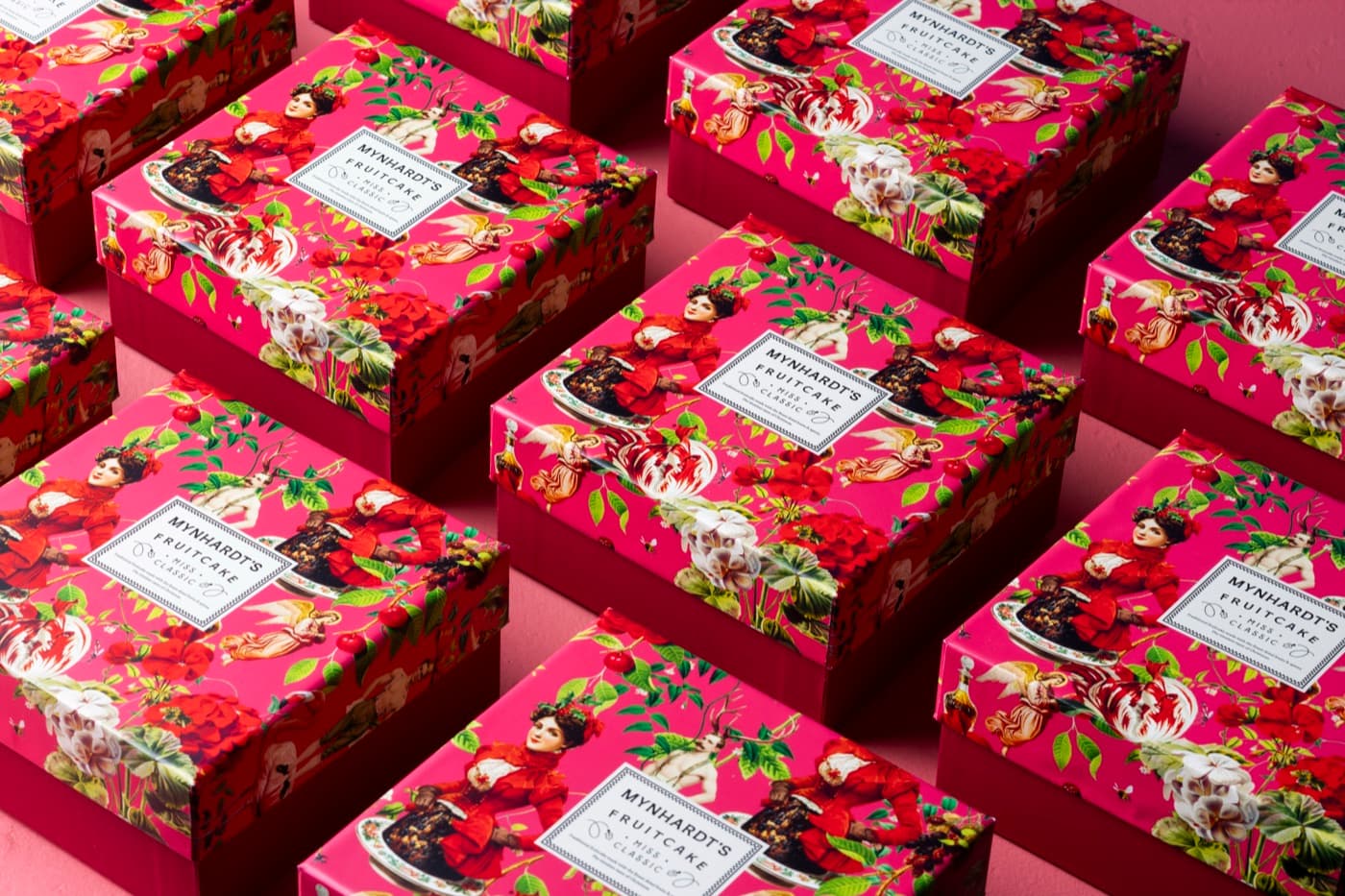 Rows of Miss Classic fruitcake boxes in hot pink illustrated wrapping, photographed from above on a pink ground