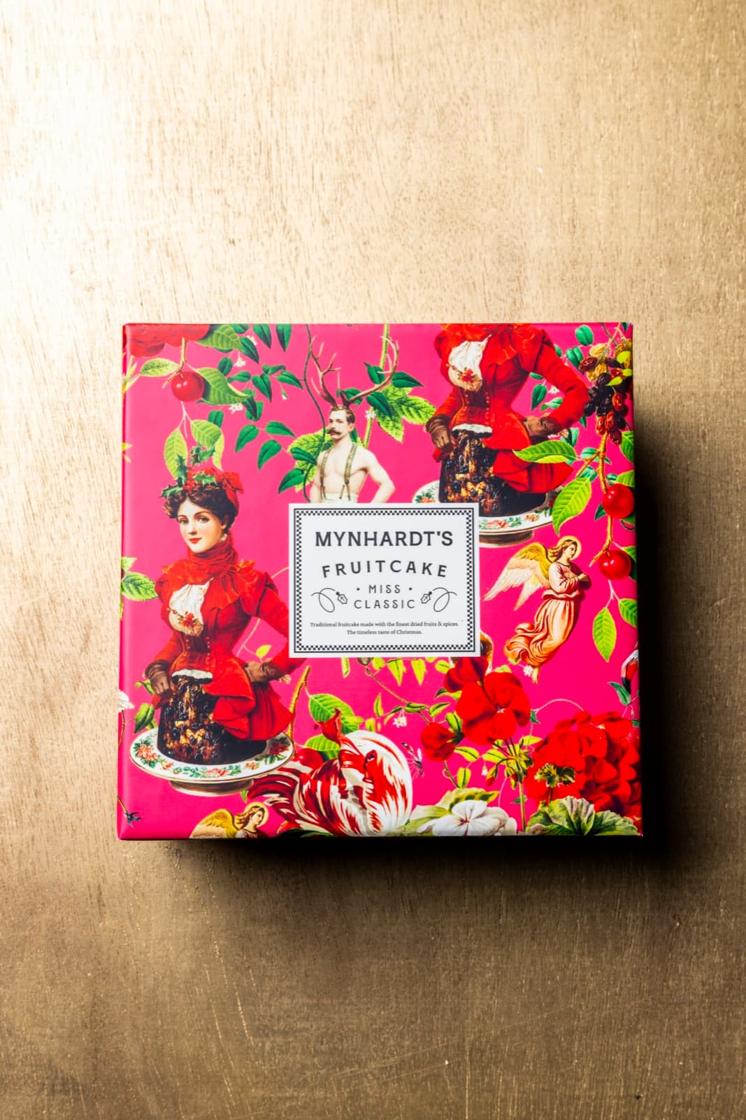 A single Miss Classic fruitcake box in hot pink illustrated wrapping, photographed on a brass surface