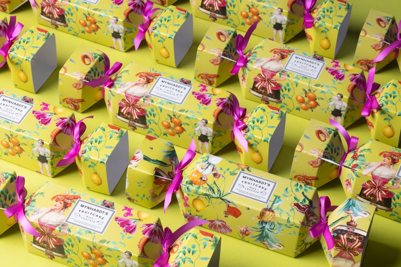 Rows of Miss Cracker fruitcakes wrapped as Christmas crackers in chartreuse paper, each tied at both ends with magenta ribbon
